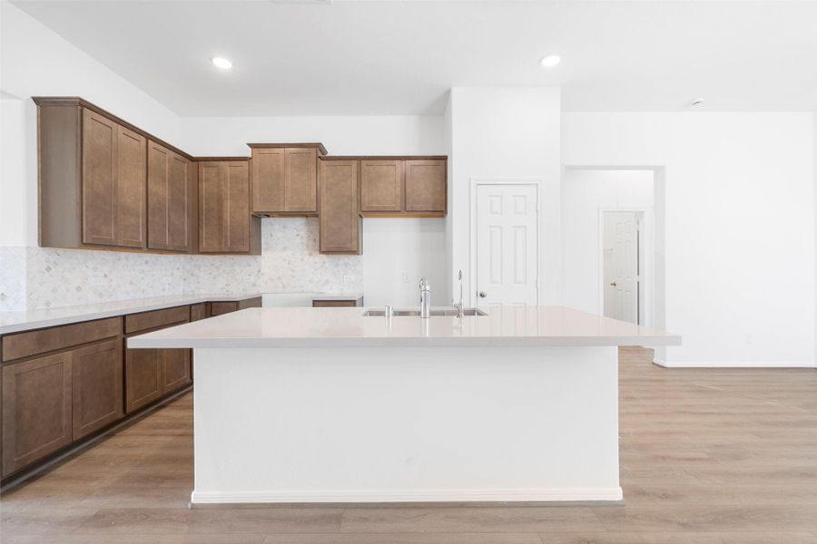 This light and bright kitchen features a large quartz island, dark stained cabinets, a large sink overlooking your family room, recessed lighting, and beautiful backsplash. This light and bright kitchen features a large quartz island, dark stained cabinets, a large sink overlooking your family room, recessed lighting, and beautiful backsplash.