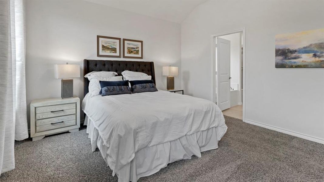 Bedroom with vaulted ceiling, light colored carpet, and ensuite bathroom