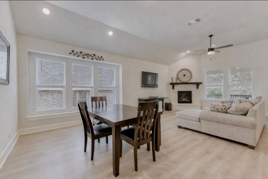 Dining area featuring a fireplace, lofted ceiling, light wood finished floors, a ceiling fan, and recessed lighting