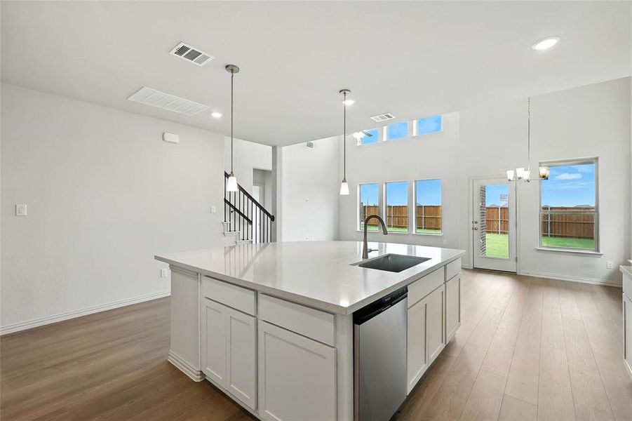 Kitchen with white cabinetry, decorative light fixtures, stainless steel dishwasher, dark wood-style flooring, and a center island with sink