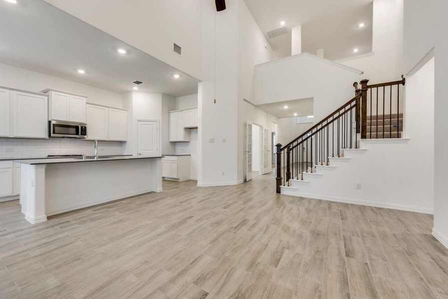 Kitchen with a towering ceiling, light wood-type flooring, white cabinets, and decorative backsplash