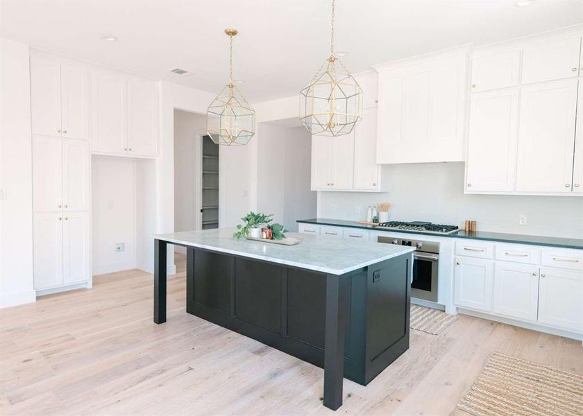 Kitchen featuring decorative light fixtures, oven, white cabinetry, a center island, and light wood-type flooring