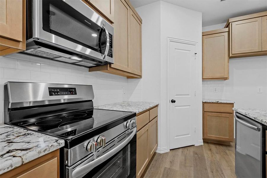 Kitchen featuring light hardwood / wood-style flooring, light brown cabinets, backsplash, and stainless steel appliances