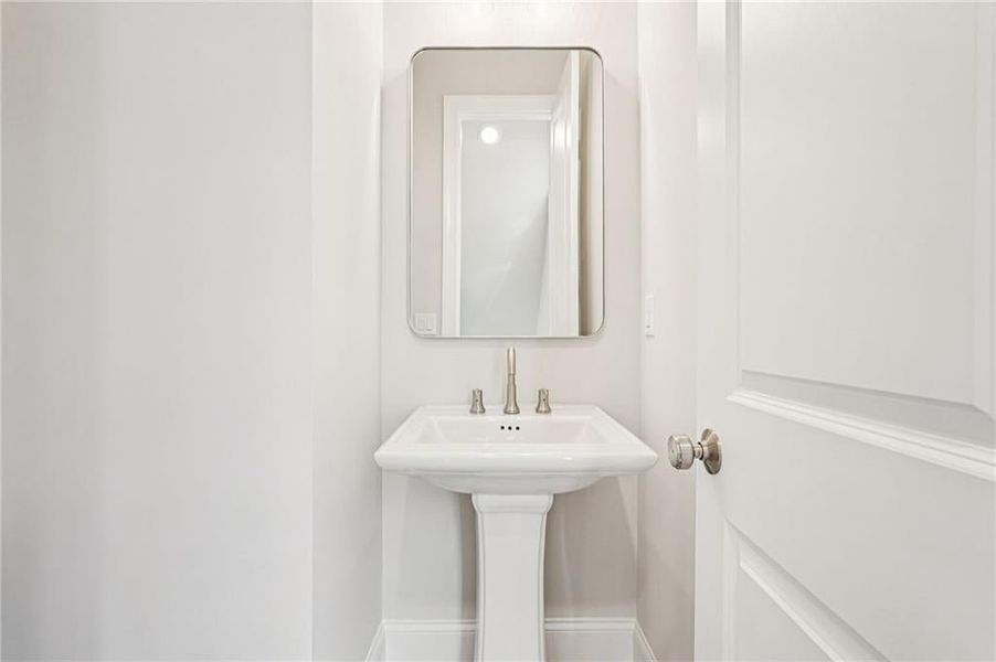 Powder bathroom on main level features brushed nickel fixtures and framed mirror to match hardware and lighting in kitchen.