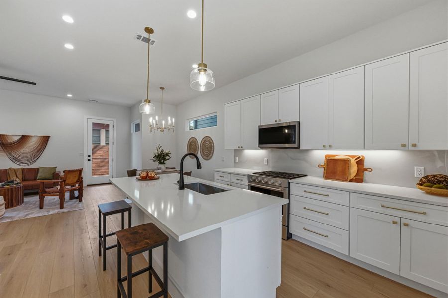 Kitchen featuring stainless steel appliances, a kitchen island with sink, white cabinetry, a breakfast bar area, and light wood-style floors