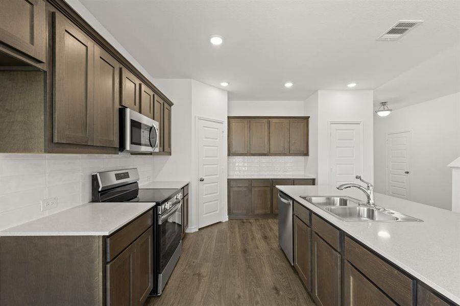 Kitchen with decorative backsplash, dark hardwood / wood-style floors, sink, dark brown cabinetry, and appliances with stainless steel finishes