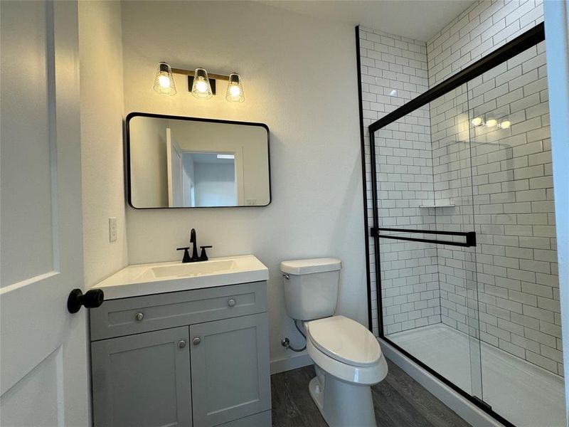 Primary Bathroom with toilet, a shower with door, vanity, and hardwood / wood-style flooring