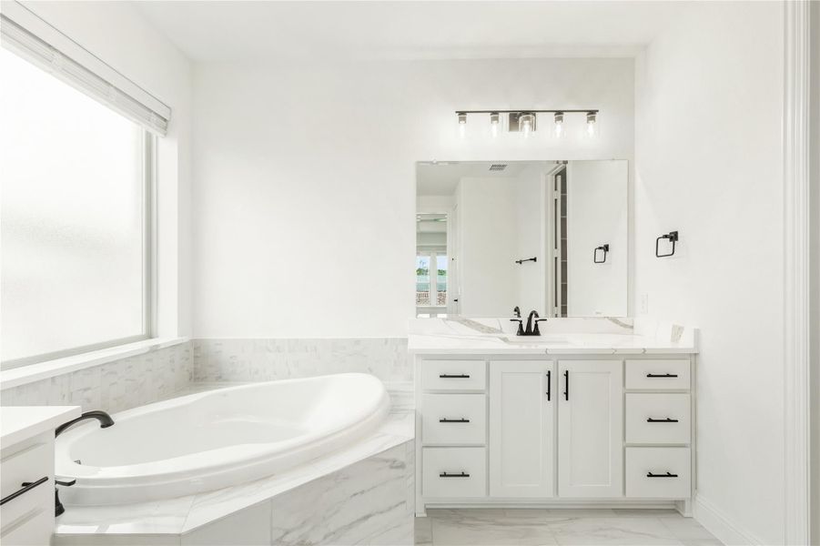 White master bathroom with soaking tub, marble tile surround, and white vanity with black hardware