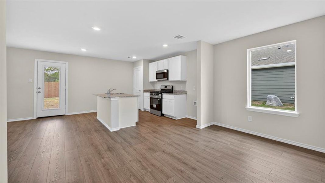 Open-concept living space featuring wood-finish flooring, a kitchen island with a built-in sink, white cabinetry, and stainless steel appliances