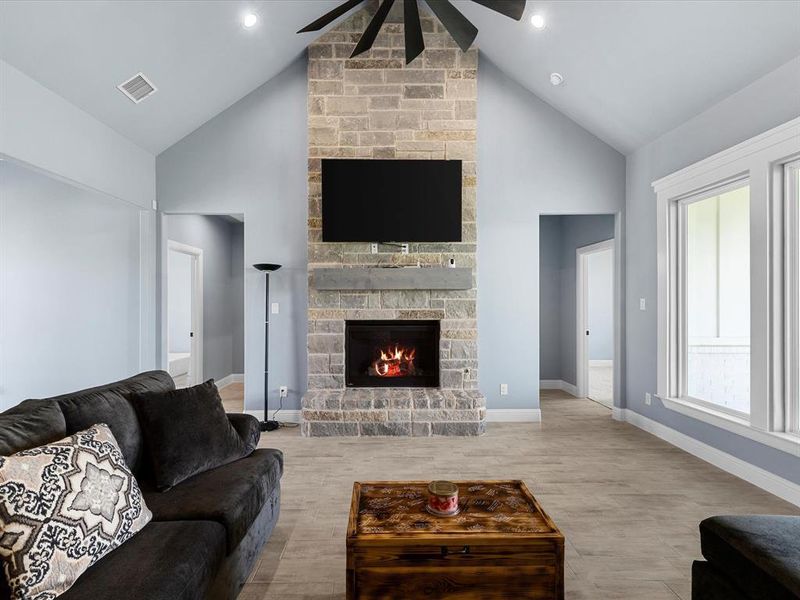 Living area with ceiling fan, high vaulted ceiling, a fireplace, and light wood-style flooring Living area with ceiling fan, high vaulted ceiling, a fireplace, and light wood-style flooring