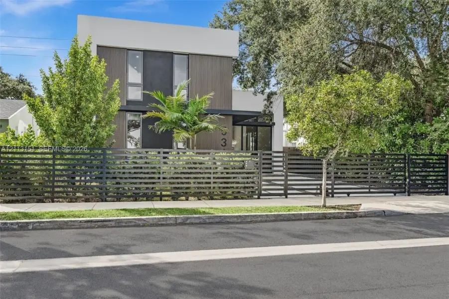 Modern architectural exterior featuring mixed-material siding, vertical rectangular windows, and a horizontal slat metal privacy fence Modern architectural exterior featuring mixed-material siding, vertical rectangular windows, and a horizontal slat metal privacy fence