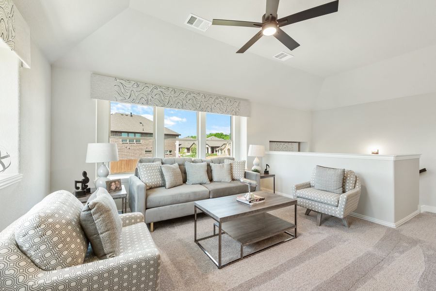 Living room with vaulted ceiling, ceiling fan, gray sofa, accent chairs, and large windows with neighborhood view