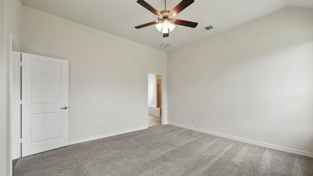 Spacious interior room featuring light gray carpeting, crisp white walls, a vaulted ceiling, and a ceiling fan with integrated lighting