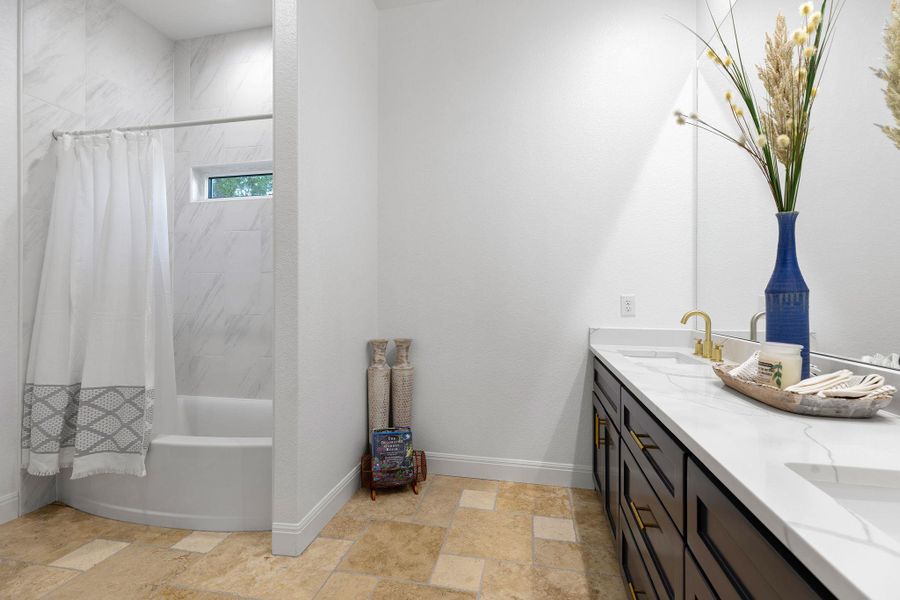 Bathroom with shower / bath combo with shower curtain, double vanity, and light stone finish floors Bathroom with shower / bath combo with shower curtain, double vanity, and light stone finish floors