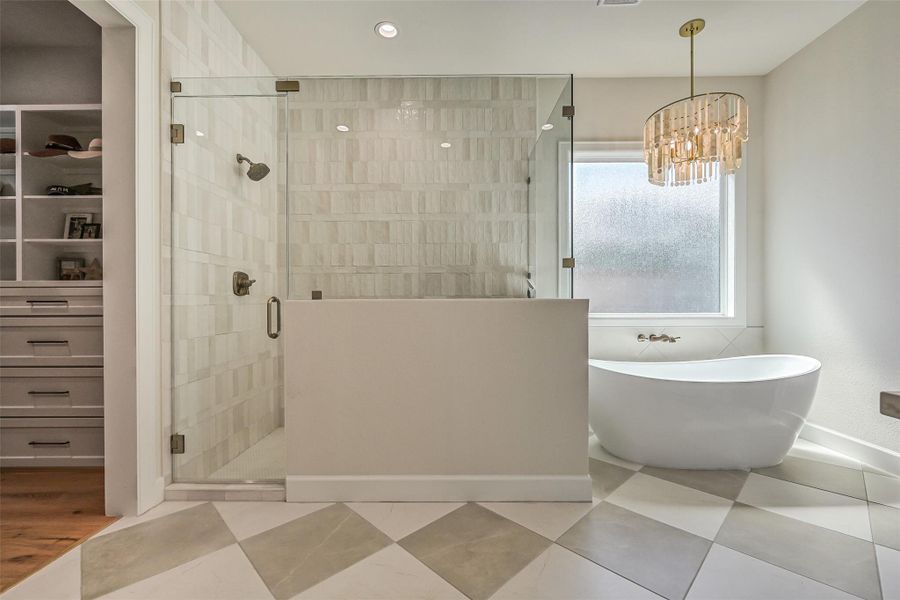 Spa-worthy primary bath pairs an oversized frameless-glass shower with floor-to-ceiling dimensional tile and a freestanding soaking tub beneath a statement chandelier, all grounded by striking large-format checkerboard flooring.