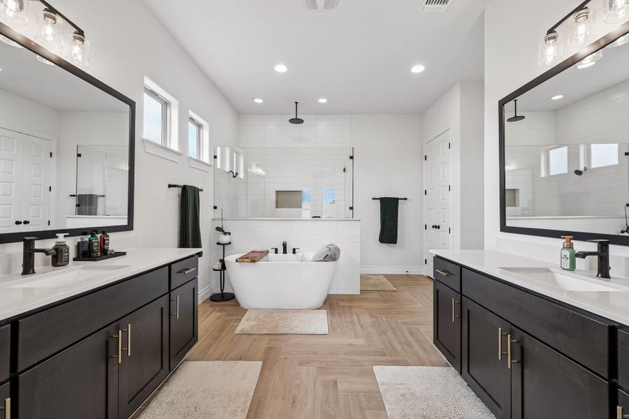 Spacious bathroom featuring dual vanities with dark cabinetry and white countertops, a freestanding soaking tub, and a separate glass-enclosed shower with white subway tile
