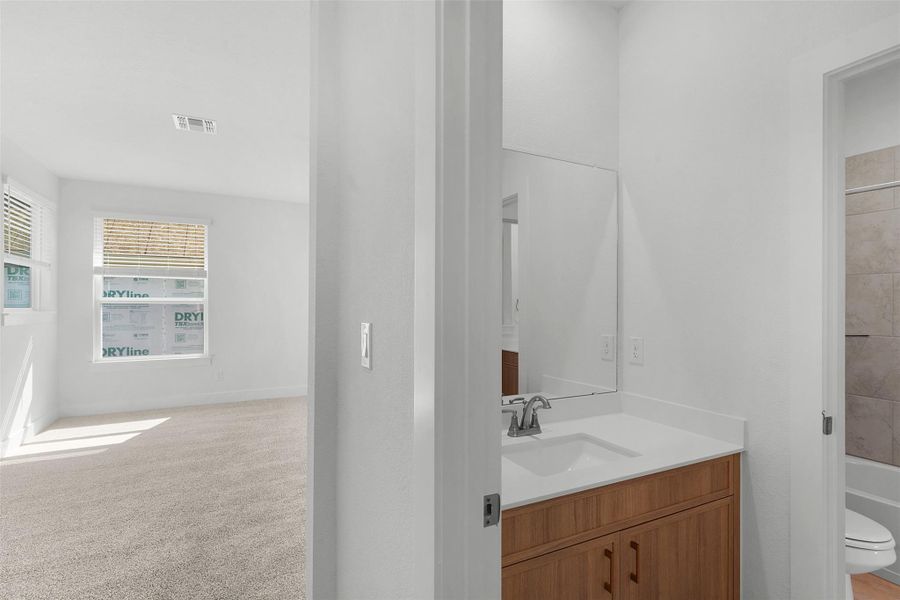 A well-lit interior offers a pristine vanity and views into a spacious, carpeted room with multiple windows.