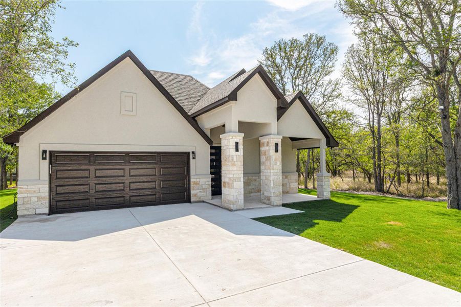 View of front of home featuring stone siding, stucco siding, concrete driveway, a front yard, and a shingled roof