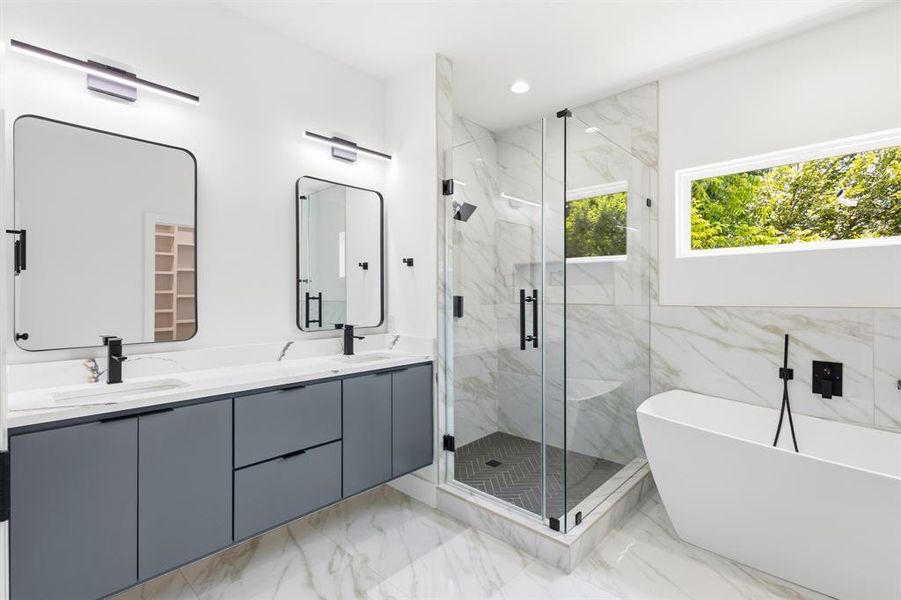 Spacious bathroom featuring a dual vanity with a white countertop and gray cabinetry, a frameless glass shower enclosure with a built-in bench, a freestanding soaking tub, and large format wall and floor tiling Spacious bathroom featuring a dual vanity with a white countertop and gray cabinetry, a frameless glass shower enclosure with a built-in bench, a freestanding soaking tub, and large format wall and floor tiling