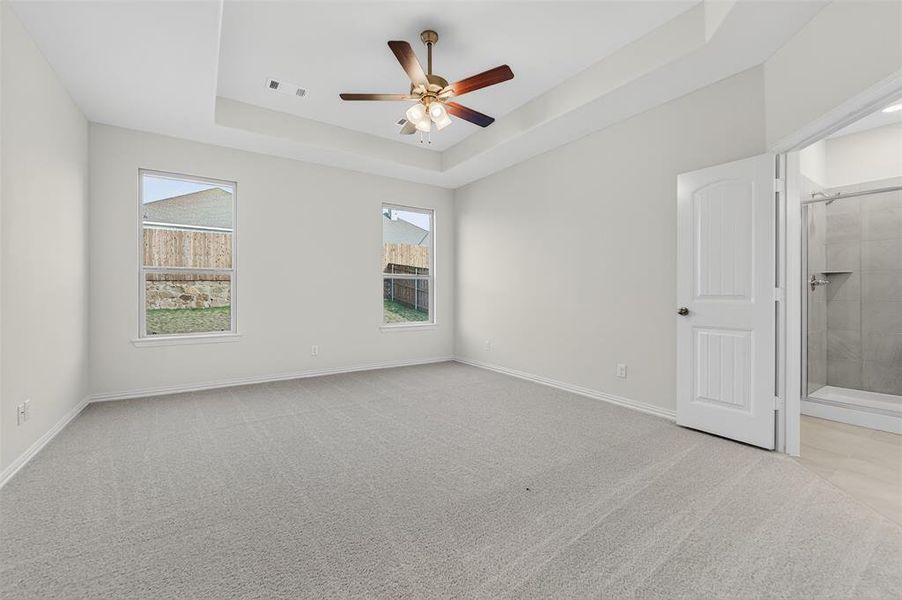 Spare room featuring a raised ceiling, light colored carpet, and ceiling fan