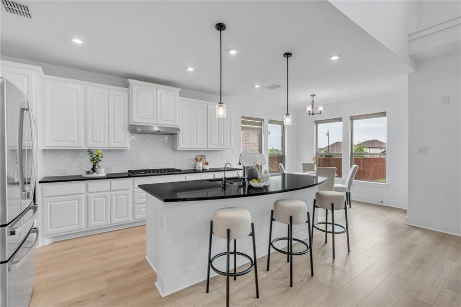 A gourmet kitchen offers bright white cabinetry, sleek black countertops, and a central island with pendant lighting.