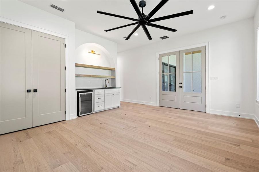 Unfurnished living room featuring french doors, recessed lighting, light wood-style flooring, wet bar, and beverage cooler