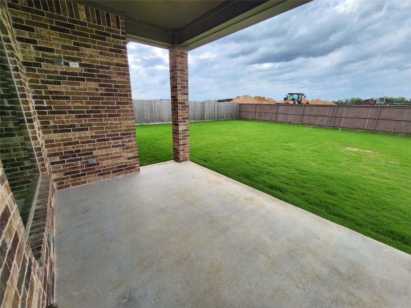 Covered concrete patio with a brick column and a spacious green lawn