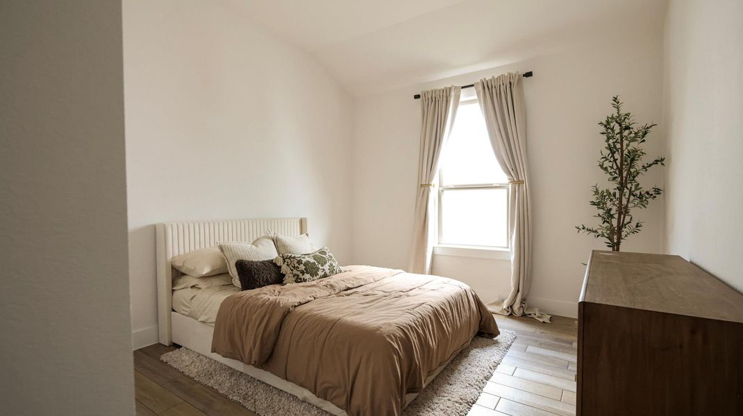A well-lit bedroom features hardwood flooring, a large window, and vaulted ceilings. A well-lit bedroom features hardwood flooring, a large window, and vaulted ceilings.