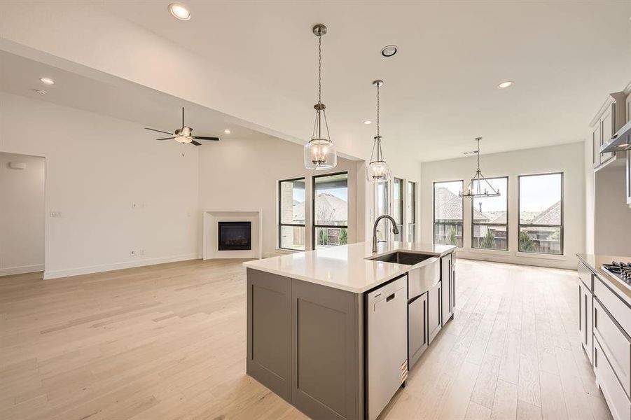 Kitchen with open floor plan, a fireplace, an island with sink, light wood-type flooring, and ceiling fan