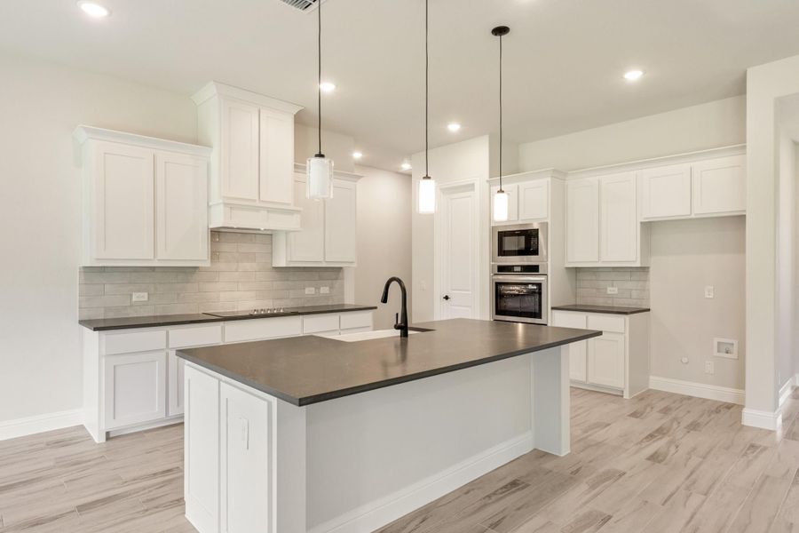 Kitchen with white cabinets, dark countertops, center island with sink, and stainless steel appliances