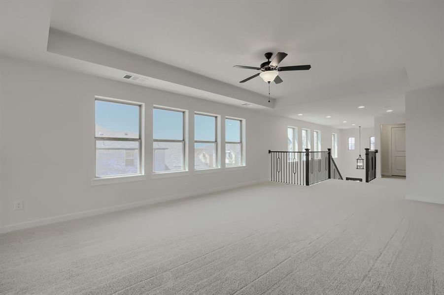 Spacious carpeted room featuring multiple windows, a ceiling fan, recessed lighting, and a staircase with a black wrought iron railing