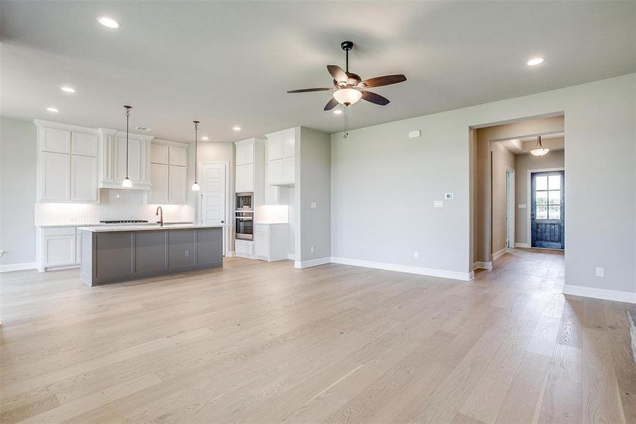 Kitchen with a kitchen island with sink, white cabinets, hanging light fixtures, light hardwood / wood-style flooring, and ceiling fan