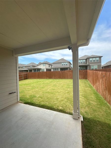 Covered concrete patio overlooking a spacious backyard with a private wood fence and manicured lawn Covered concrete patio overlooking a spacious backyard with a private wood fence and manicured lawn