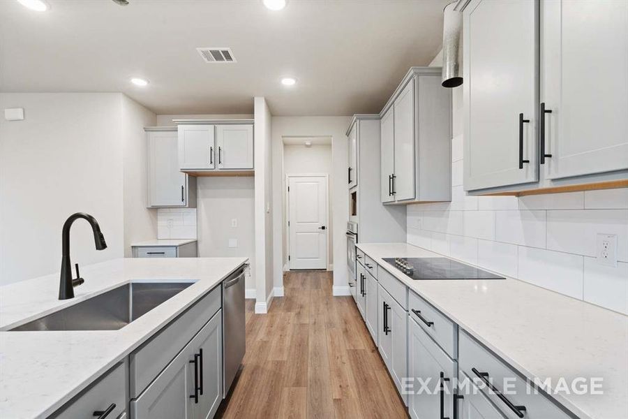 Kitchen with sink, tasteful backsplash, light stone counters, light hardwood / wood-style floors, and appliances with stainless steel finishes