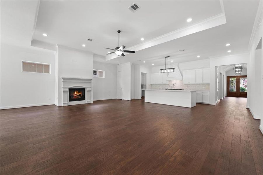 This is a spacious, modern open-concept living area with hardwood floors, featuring a large kitchen with white cabinetry and an island, as well as a cozy fireplace. High ceilings and ample lighting create an inviting atmosphere.