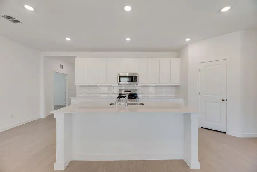Kitchen with backsplash, light countertops, light wood-style floors, appliances with stainless steel finishes, and white cabinets