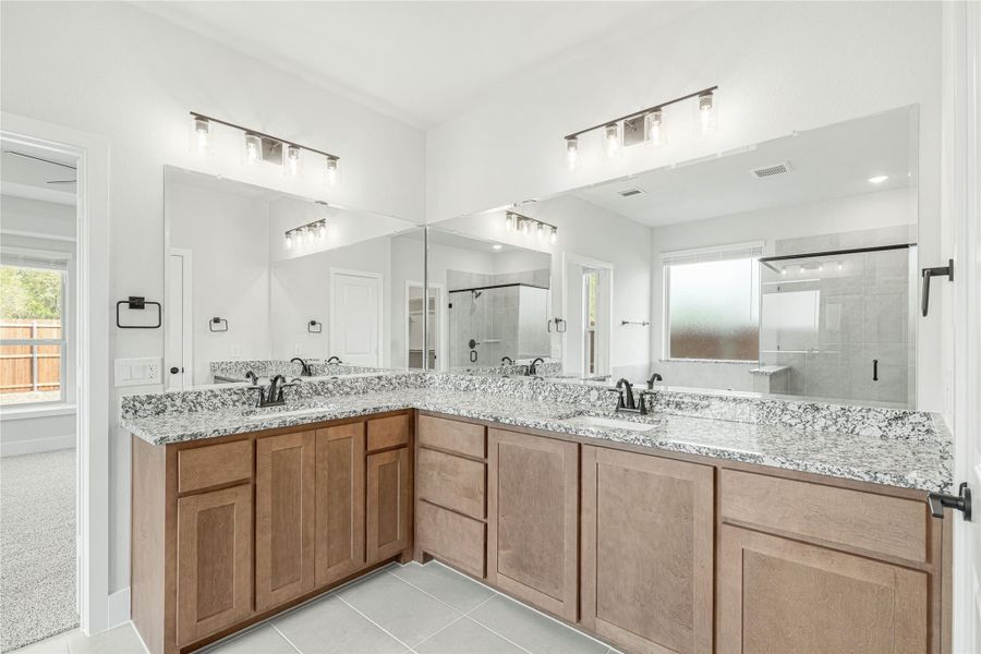 Master bathroom with L-shaped double vanity, granite countertops, wood cabinets, and walk-in shower visible in mirror reflection.