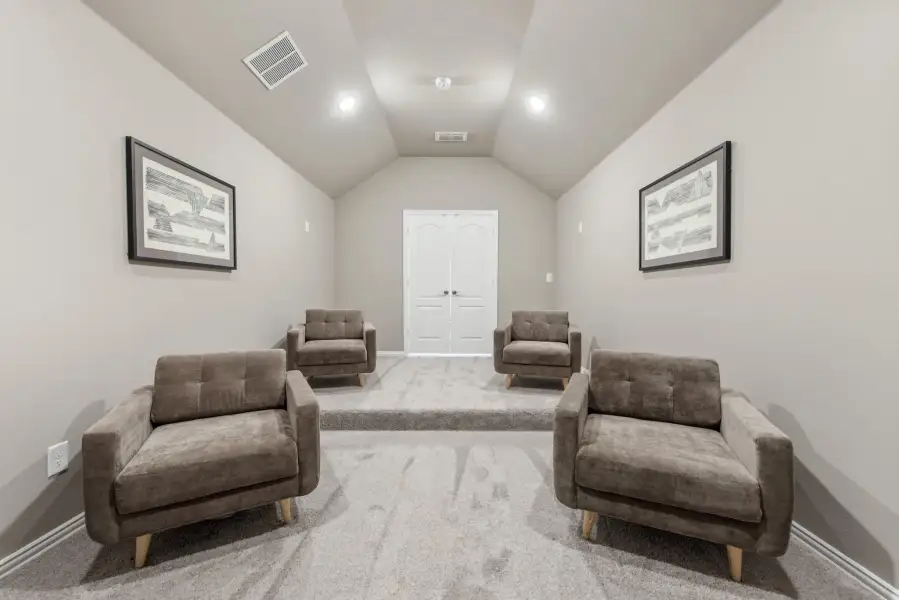 Bonus room with vaulted ceiling, four brown armchairs, carpet flooring, and framed wall art