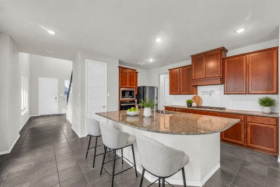 A well-appointed kitchen includes an expansive curved breakfast bar island, matching wood cabinetry, dark tile floors, and a modern subway tile backsplash.**Virtually staged A well-appointed kitchen includes an expansive curved breakfast bar island, matching wood cabinetry, dark tile floors, and a modern subway tile backsplash.**Virtually staged