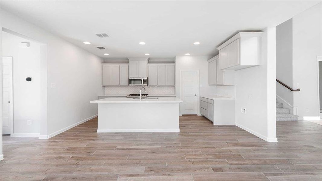 Kitchen featuring backsplash, sink, light wood-type flooring, and a kitchen island with sink