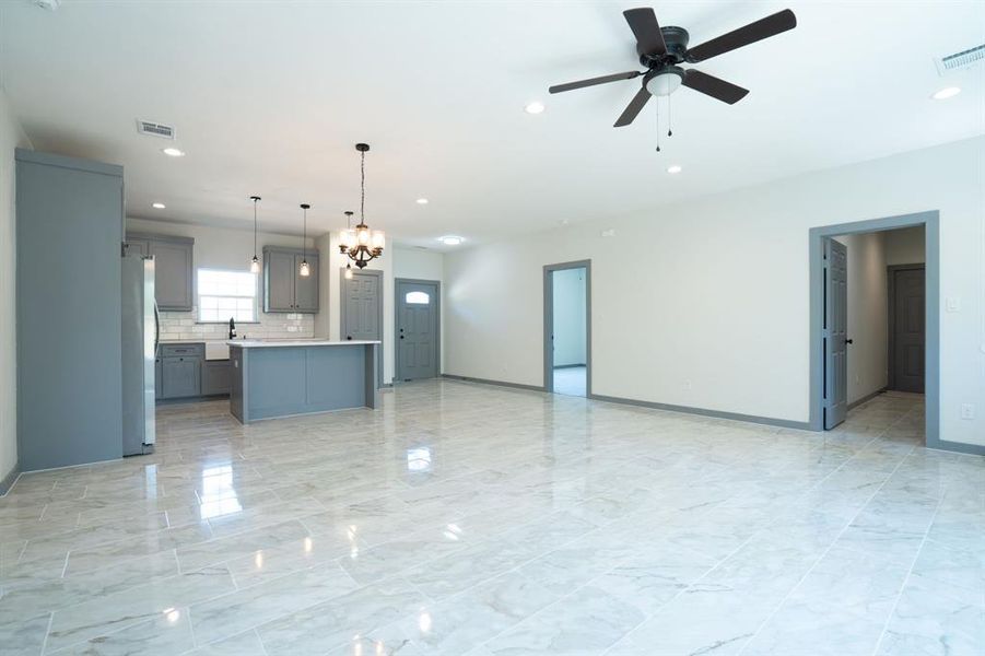 Kitchen with light tile patterned flooring, a center island, ceiling fan with notable chandelier, stainless steel refrigerator, and pendant lighting