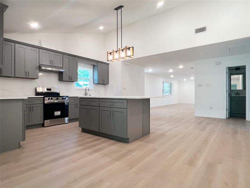 Open-concept kitchen featuring grey cabinetry, stainless steel range, white countertops, and a central island with pendant lighting