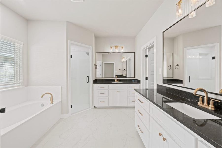 Full bath with two vanities, a stall shower, a garden tub, and light marble finish floors