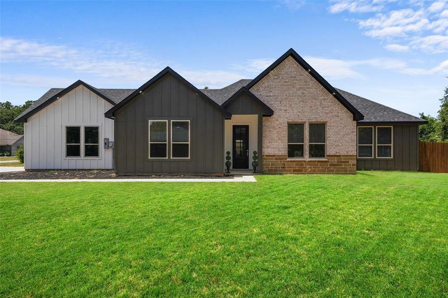 Contemporary exterior featuring a brick facade with stone detailing, dark siding, white board and batten accents, a black shingle roof, and a dark front door Contemporary exterior featuring a brick facade with stone detailing, dark siding, white board and batten accents, a black shingle roof, and a dark front door