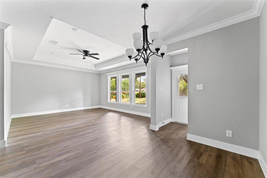 Unfurnished living room with ornamental molding, a chandelier, dark wood-style flooring, a raised ceiling, and ceiling fan