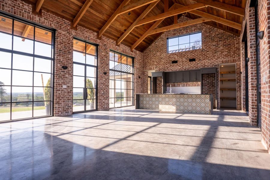 Unfurnished living room featuring brick wall, finished concrete floors, and a high wood beamed ceiling