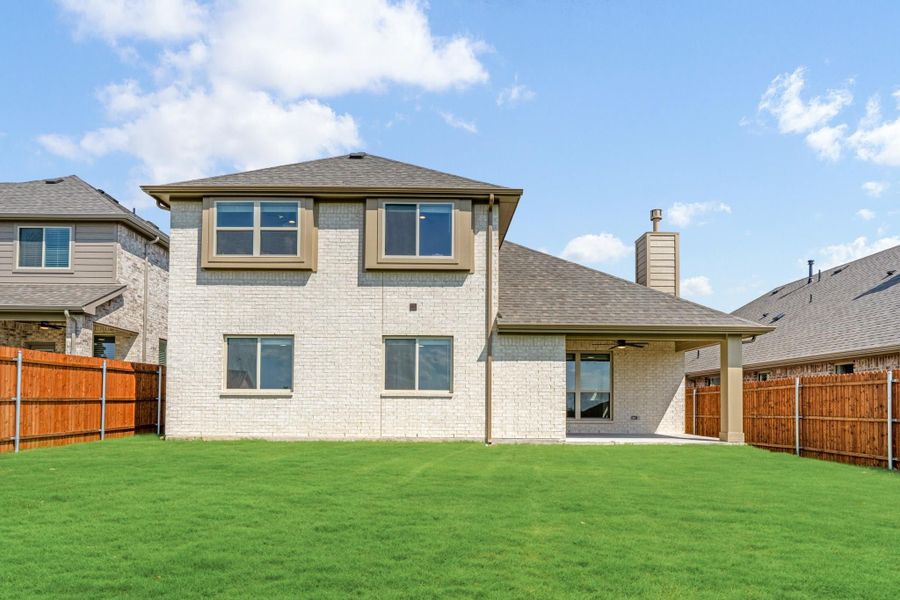 Two-story home with white brick exterior, covered patio, and fenced backyard with green lawn