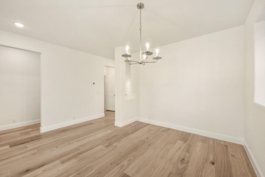 Empty dining room with light wood floors, white walls, and a silver chandelier Empty dining room with light wood floors, white walls, and a silver chandelier