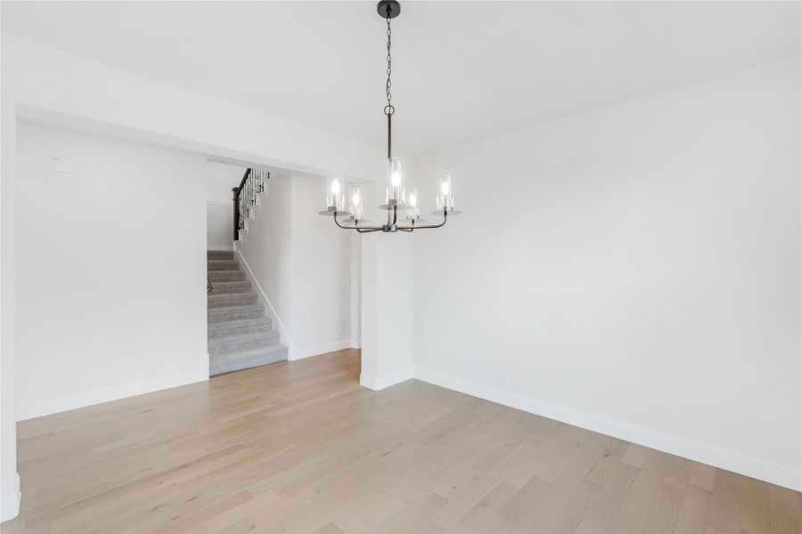Empty dining room with light hardwood floors, black chandelier, and staircase visible in background Empty dining room with light hardwood floors, black chandelier, and staircase visible in background