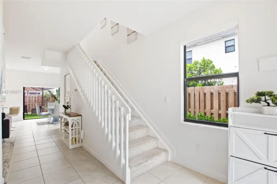 Interior staircase with white wood railing and carpeted treads, complemented by ceramic tile flooring and a large black-trimmed window